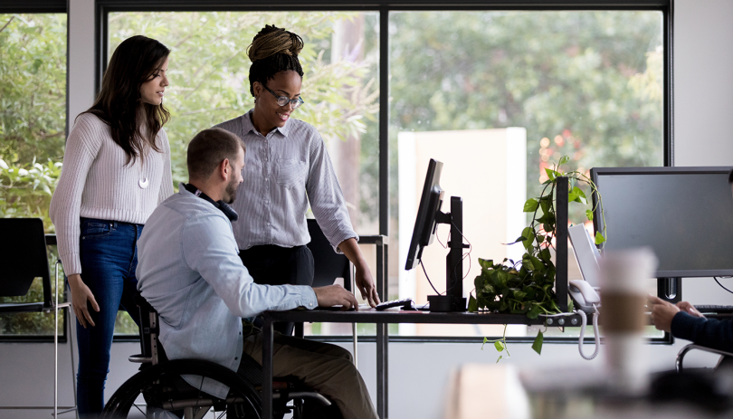 2 Woman 1 man in wheelchair working at desk_1400x800